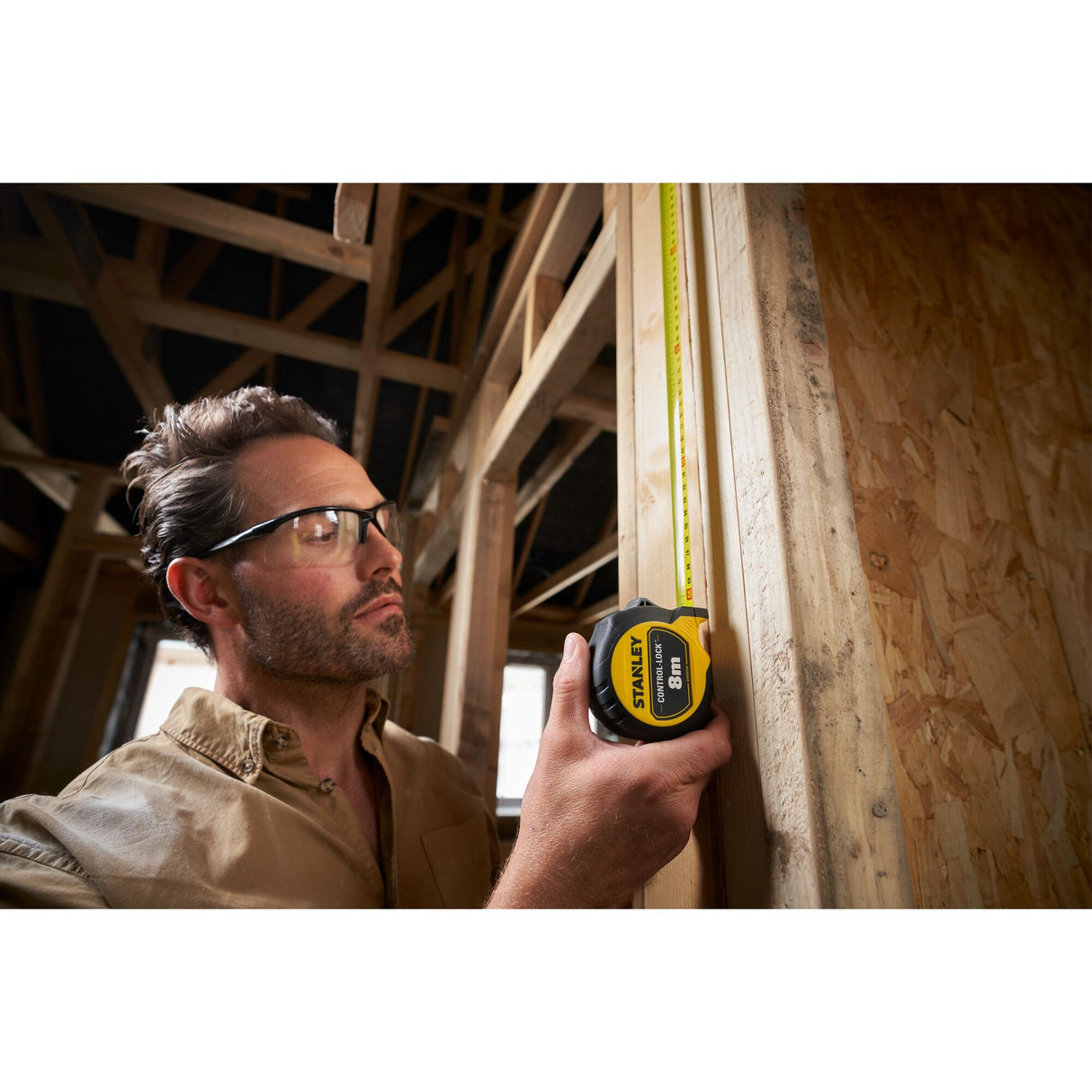 Mètre ruban Stanley, outil de mesure jaune et noir, utilisé sur un chantier de construction bois.