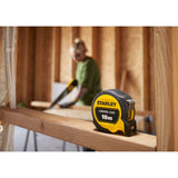 Mètre ruban Stanley noir et jaune, outil de mesure, 10m, sur chantier de construction.