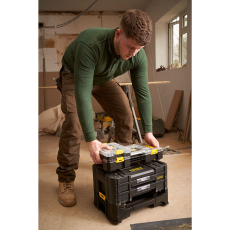 Homme manipulant une boîte à outils noire Stanley, type rangement modulaire, couleur noire avec détails jaunes