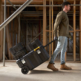 Homme tirant une mallette à outils Stanley noire sur chantier, marque visible, couleur noire.