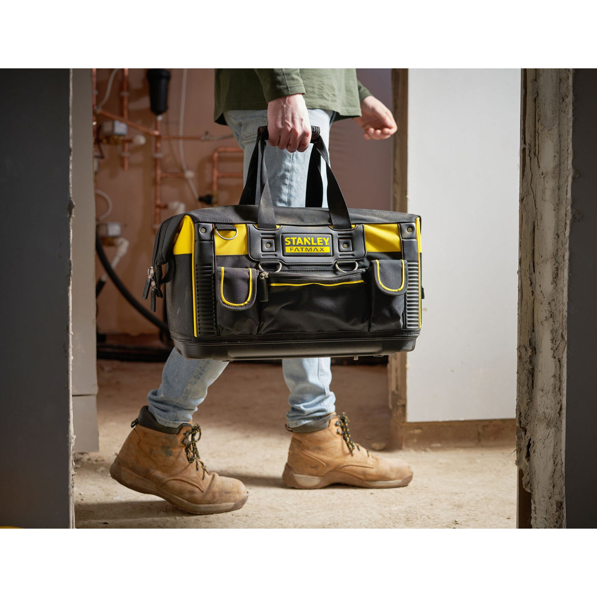 Sac à outils Stanley FatMax noir et jaune porté par un artisan, sacoche de chantier robuste.