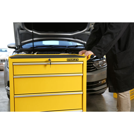 Servante d’atelier Stanley jaune avec tiroirs devant une voiture, outil de rangement professionnel.