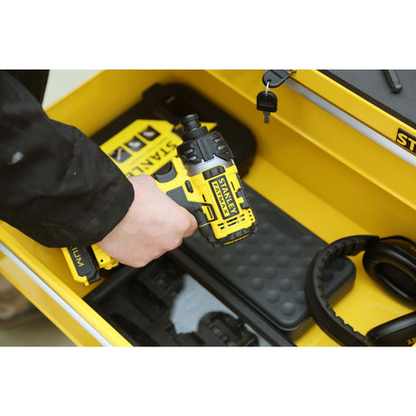 Visseuse sans fil Stanley jaune et noire, tenue à la main, dans un coffret à outils.