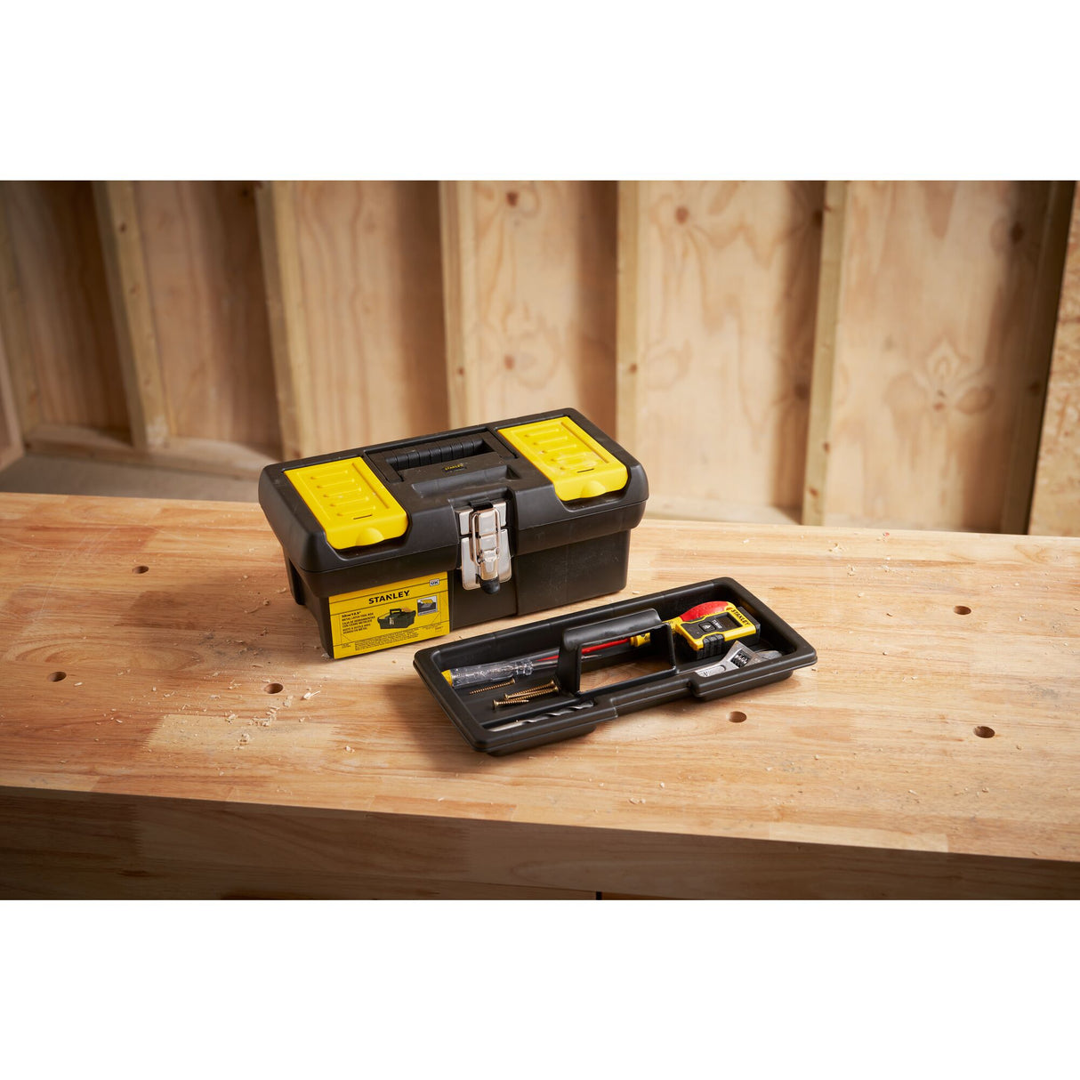 Boîte à outils Stanley noire et jaune, vide, posée sur un établi en bois.