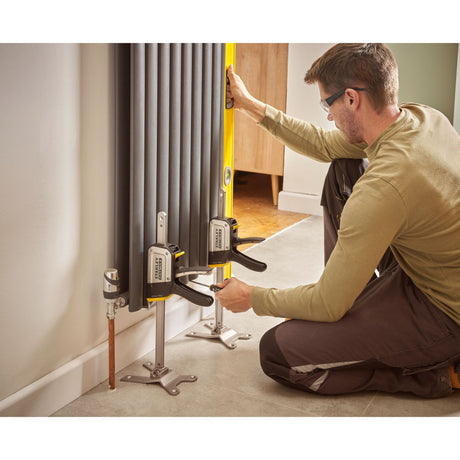 Homme utilisant des serre-joints gris Stanley pour installer un radiateur gris.
