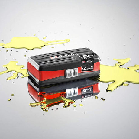 Boîte à outils Facom, type R2nano, couleur noire et rouge, posée sur une surface avec éclaboussures jaunes.