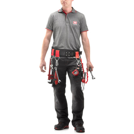Homme portant une ceinture porte-outils Facom noire et rouge avec outils, pantalon noir, polo gris.