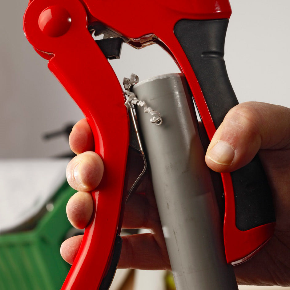 Coupe-tube Facom rouge découpant un tuyau gris, outillage plomberie