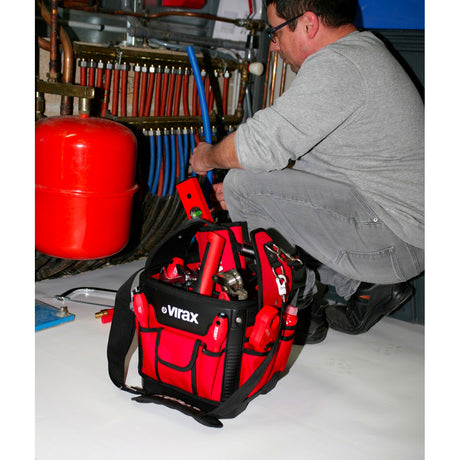 Sac à outils Virax rouge pour plombier, utilisé sur un chantier de plomberie.