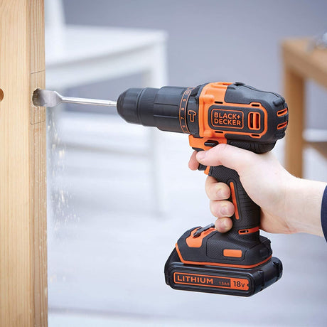 Perceuse sans fil Black+Decker noire et orange, 18V, en action sur du bois.