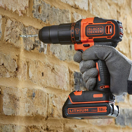 Perceuse sans fil BLACK+DECKER, outil électroportatif noir et orange, en action sur mur.
