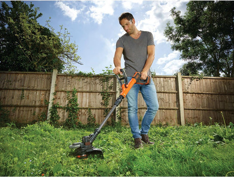 Coupe-bordures Black & Decker orange utilisé dans un jardin, outil de jardinage électrique
