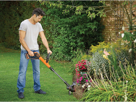 Homme utilisant un coupe-bordure Black+Decker orange pour jardinage sur pelouse
