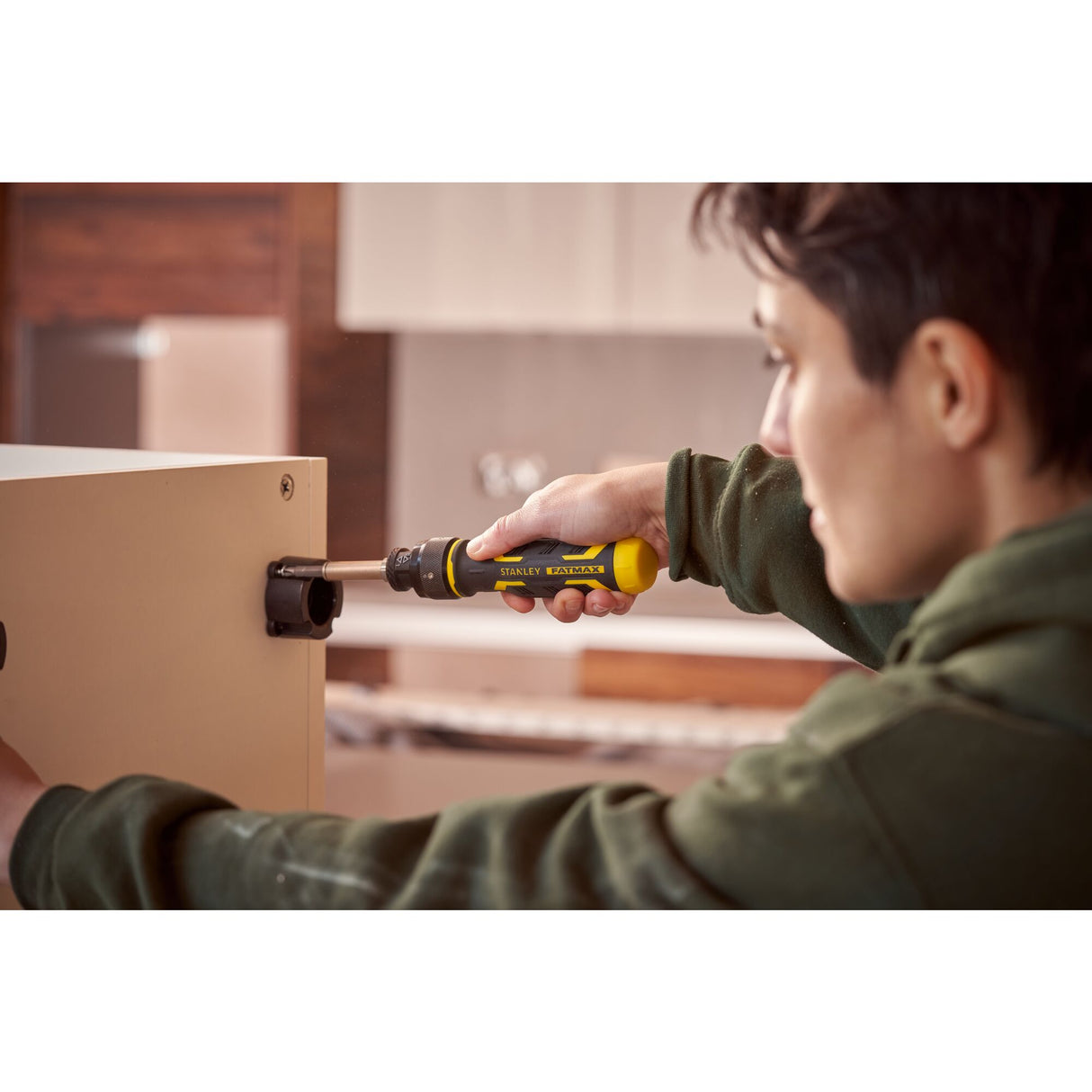 Tournevis jaune Stanley FATMAX utilisé par une personne sur un meuble beige.