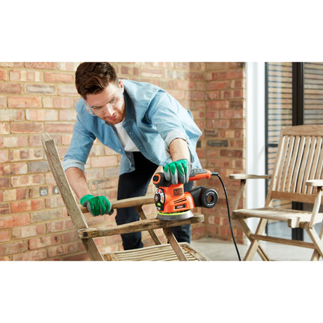 Homme utilisant une ponceuse orange Black+Decker, ponçage bois, outil électrique, couleur orange