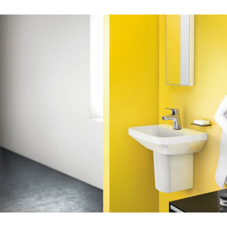 Lavabo blanc Grohe, type mural, sur mur jaune, avec robinet chrome.