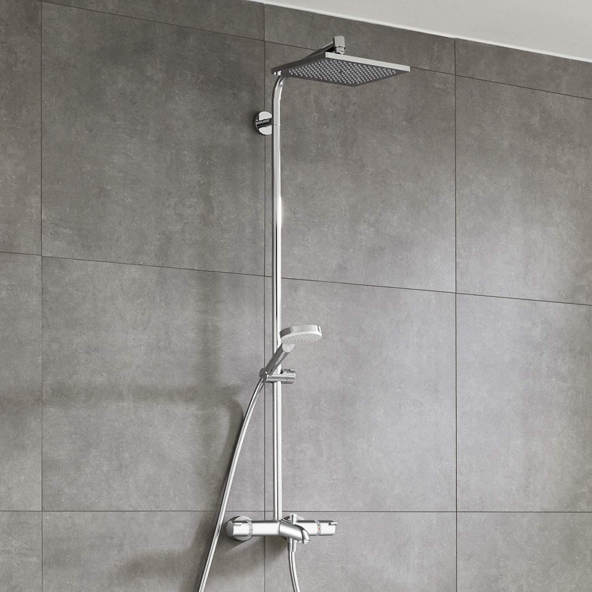 Colonne de douche Grohe, chromée, moderne avec pommeau carré et douchette, sur carrelage gris.