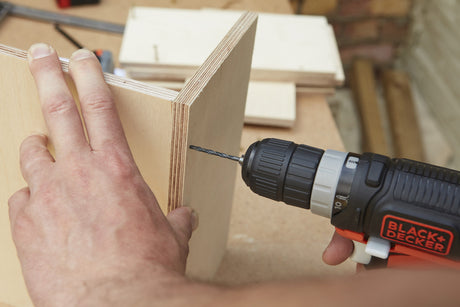 Perceuse électrique Black+Decker noire et orange, outil électroportatif en action sur bois clair