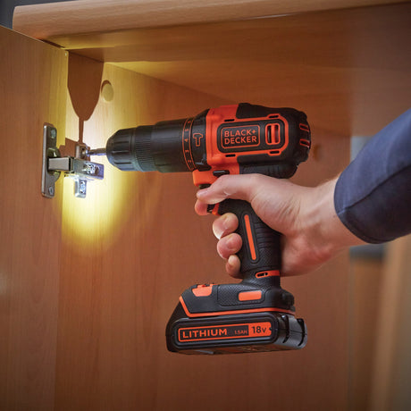 Perceuse visseuse sans fil BLACK+DECKER, noir et orange, utilisée sur une charnière de meuble