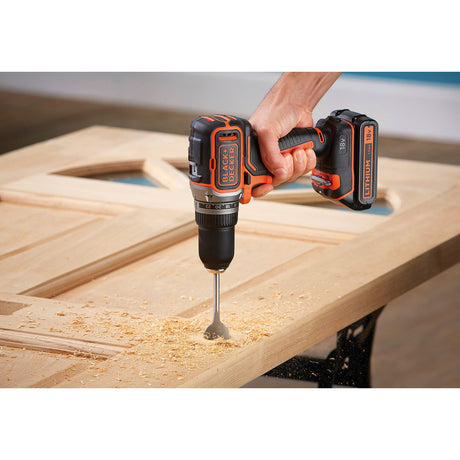 Perceuse sans fil Black+Decker, outil électroportatif noir et orange, en action sur bois
