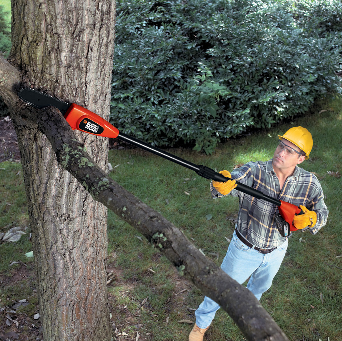 Élagueuse télescopique Black+Decker orange et noire utilisée pour couper une branche d’arbre.