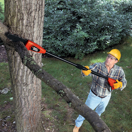 Élagueuse télescopique Black+Decker orange et noire utilisée pour couper une branche d’arbre.