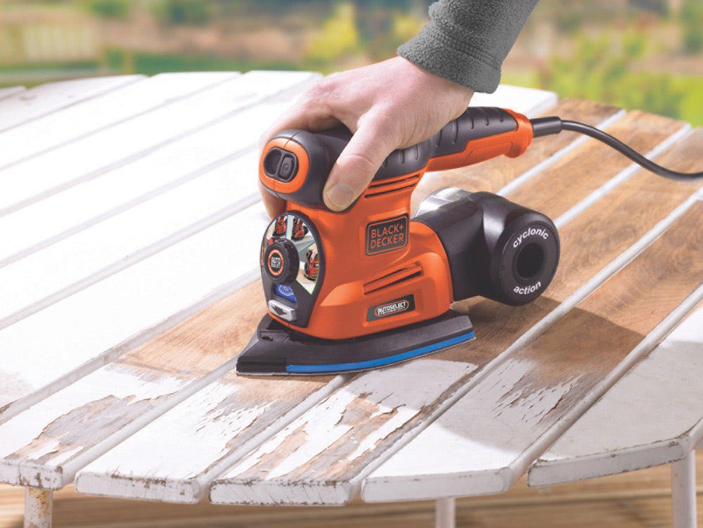 Ponceuse électrique Black+Decker orange utilisée sur une table en bois