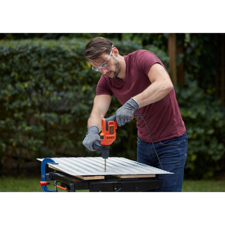 Perceuse électrique Black+Decker orange, outil de bricolage, utilisée en extérieur.