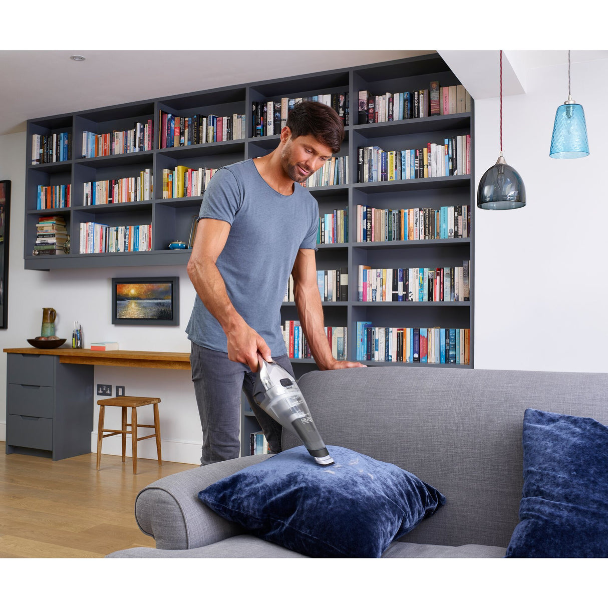 Aspirateur à main Black+Decker, gris, utilisé sur un canapé dans un salon moderne