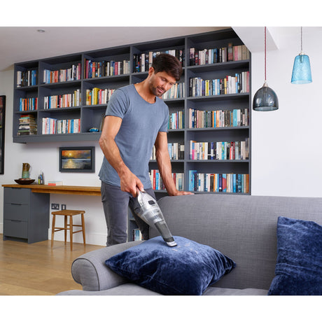 Aspirateur à main Black+Decker, gris, utilisé sur un canapé dans un salon moderne