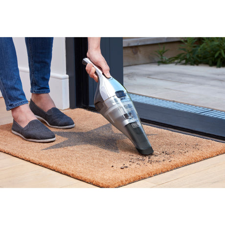 Aspirateur à main Black+Decker, électrique, couleur gris argent, utilisé sur un paillasson
