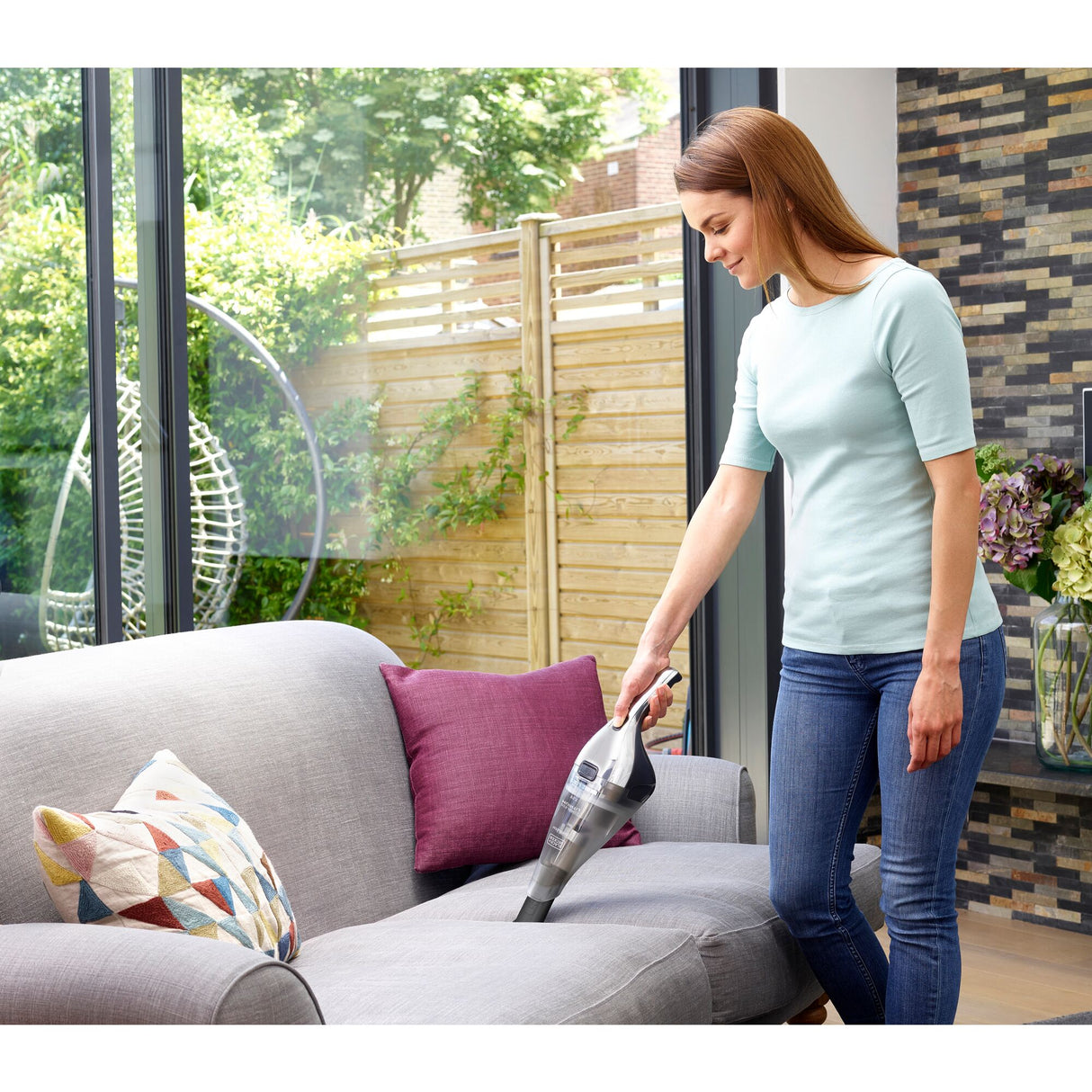 Aspirateur à main Black+Decker, modèle portable, couleur gris, utilisé sur un canapé.