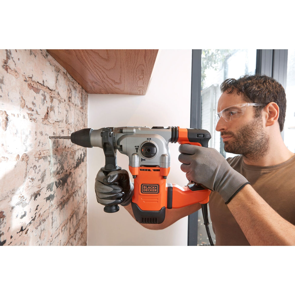 Perforateur burineur Black+Decker orange et gris utilisé sur un mur en briques