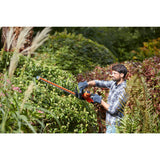 Homme utilisant un taille-haie Black+Decker orange pour tailler des haies vertes dans un jardin.