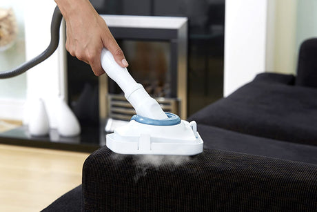 Nettoyeur vapeur blanc et bleu marque Vax, appareil électroménager sur canapé foncé.