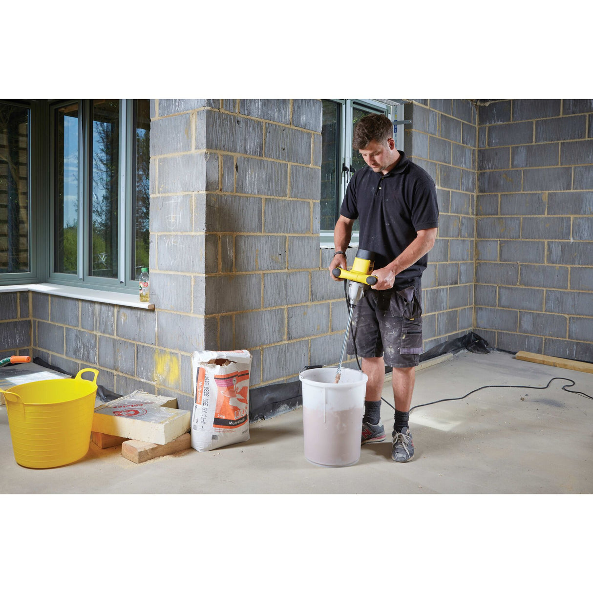 Homme utilisant un mélangeur Rubi, outil électrique jaune, sur un chantier de construction