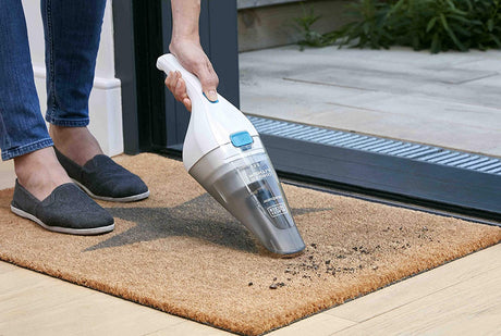 Aspirateur à main Black+Decker, blanc et gris, utilisé pour nettoyer un paillasson.
