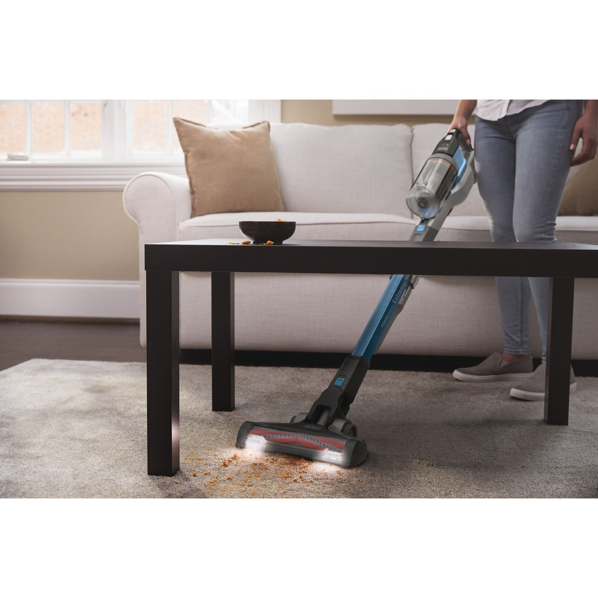 Aspirateur balai Bissell bleu nettoyant des miettes sur moquette dans un salon moderne