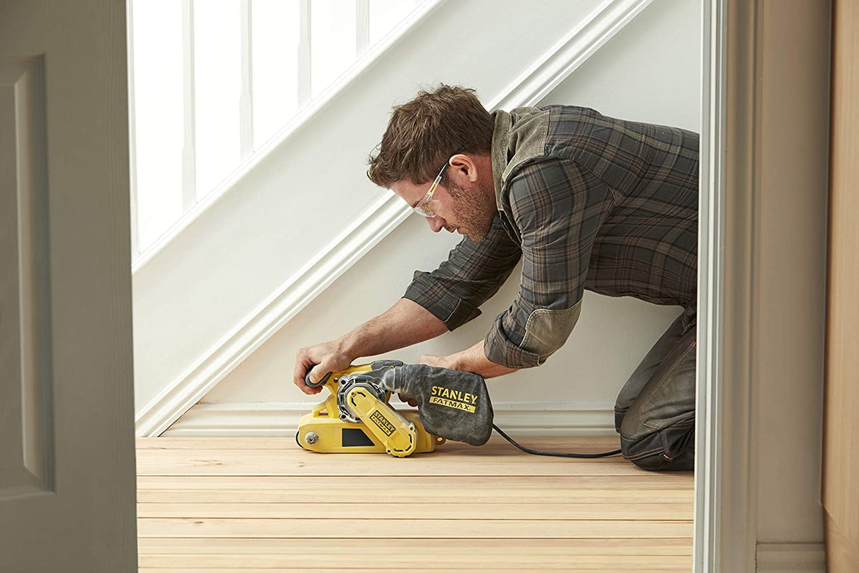 Homme utilisant une ponceuse à bande Stanley Fatmax jaune sur parquet clair.