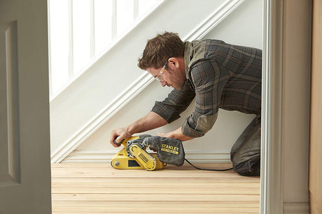 Homme utilisant une ponceuse à bande Stanley Fatmax jaune sur parquet clair.