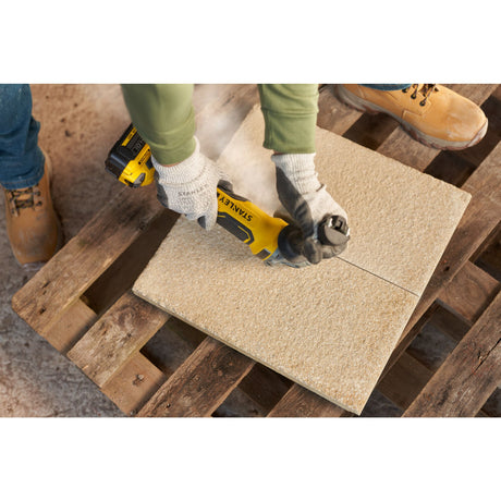 Meuleuse Stanley jaune découpant une dalle beige, outil électroportatif de couleur jaune.