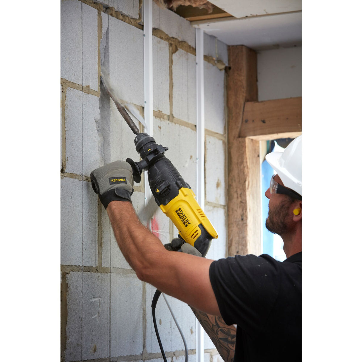 Homme utilisant une scie sabre jaune Stanley sur un mur en béton, outil électroportatif noir et jaune