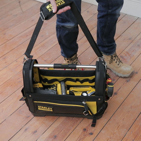 Sac à outils Stanley FATMAX noir et jaune, porté par une personne sur un sol en bois.