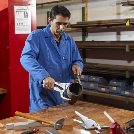 Hommes utilisant une pince Facom, outil de plomberie argenté, sur un tuyau foncé en atelier.