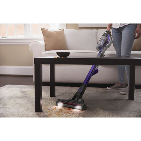 Aspirateur balai Bissell violet en action sur tapis, nettoyage sous une table basse.